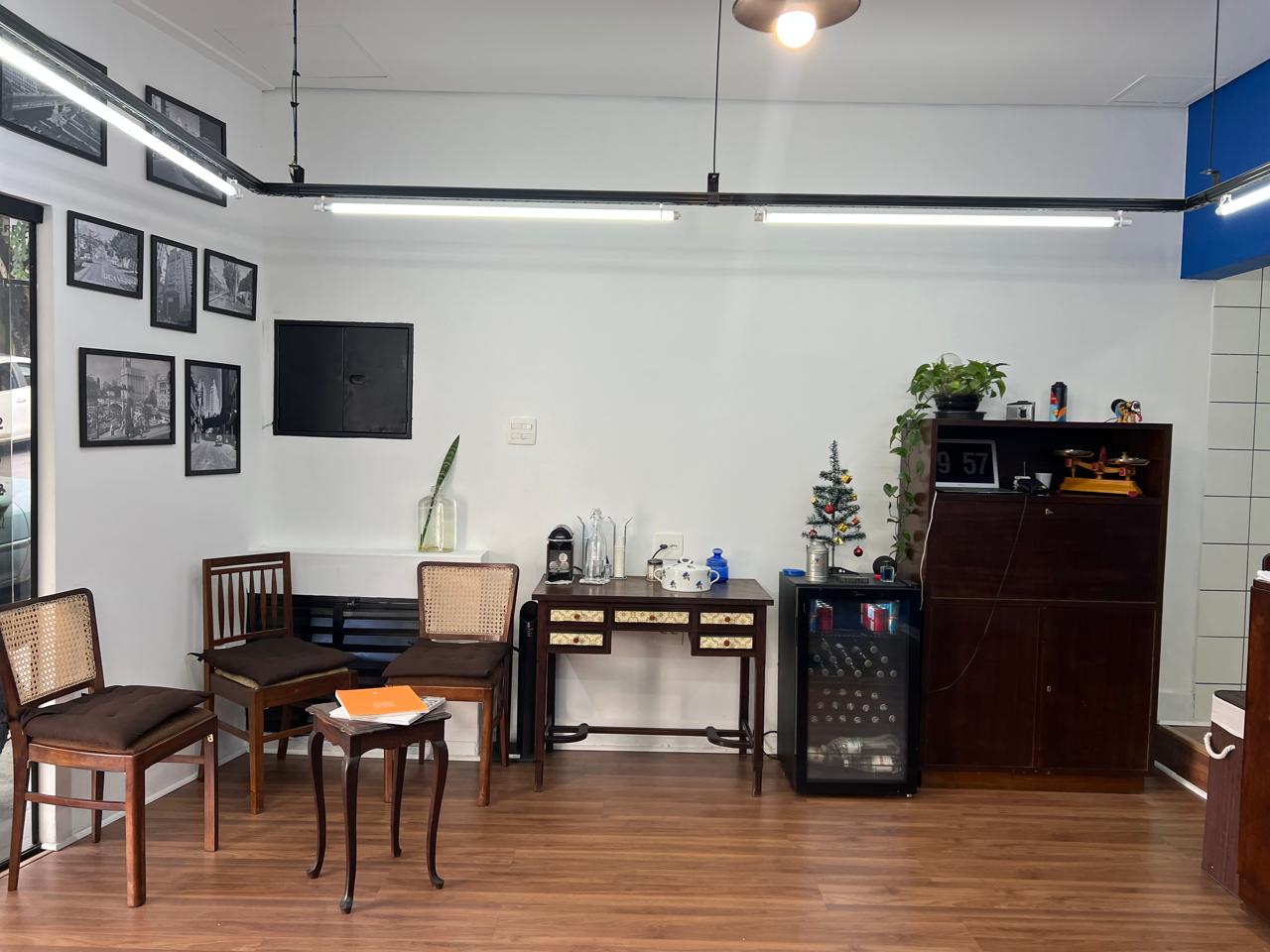 Sala de espera da Vila Barbearia: cadeiras de palhinha, mesa de madeira e fotos antigas de São Paulo na parede