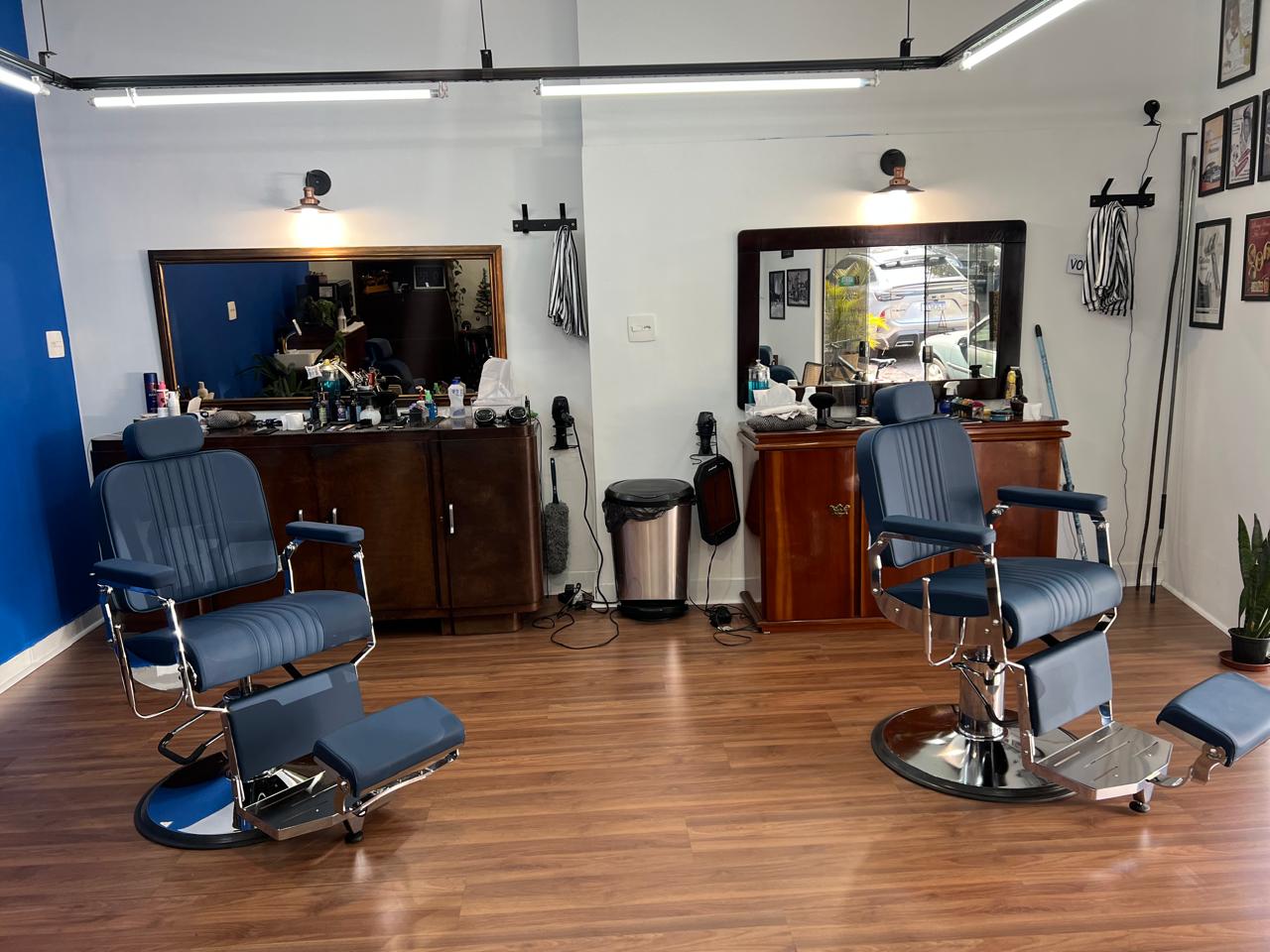 Interior da Vila Barbearia: duas cadeiras de barbeiro em couro azul, parede cobalto e móveis de madeira